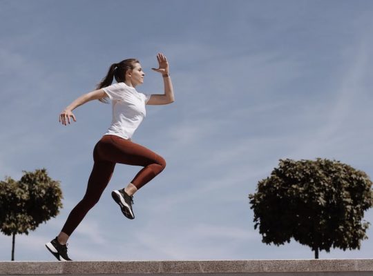 Athletic woman running on an outdoor road, demonstrating fitness and determination under a blue sky.