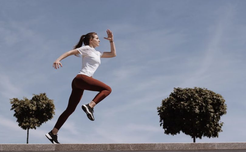 Athletic woman running on an outdoor road, demonstrating fitness and determination under a blue sky.